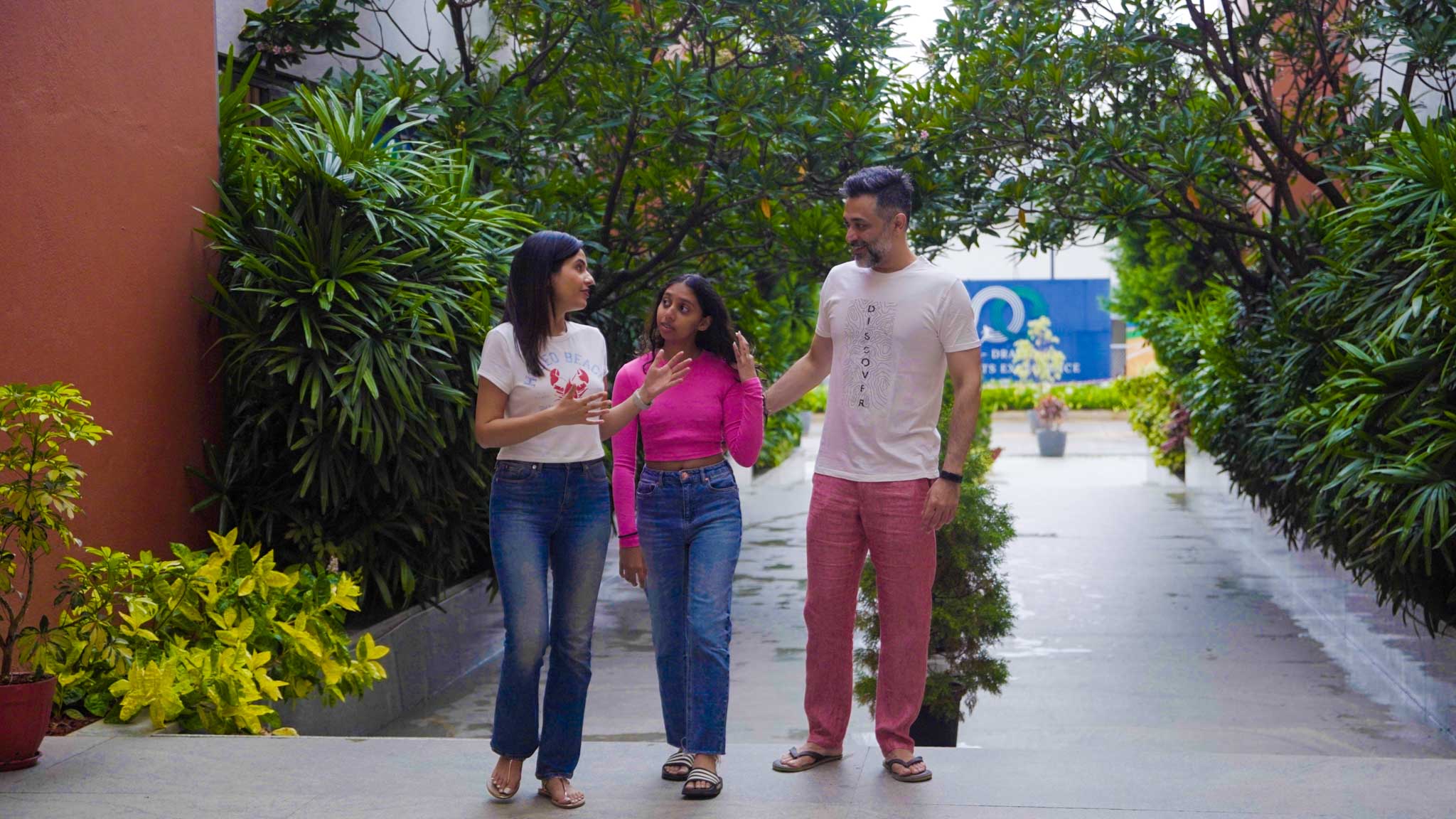 Family of two adults and one kid walking and chatting outdoors along a pathway surrounded by greenery.